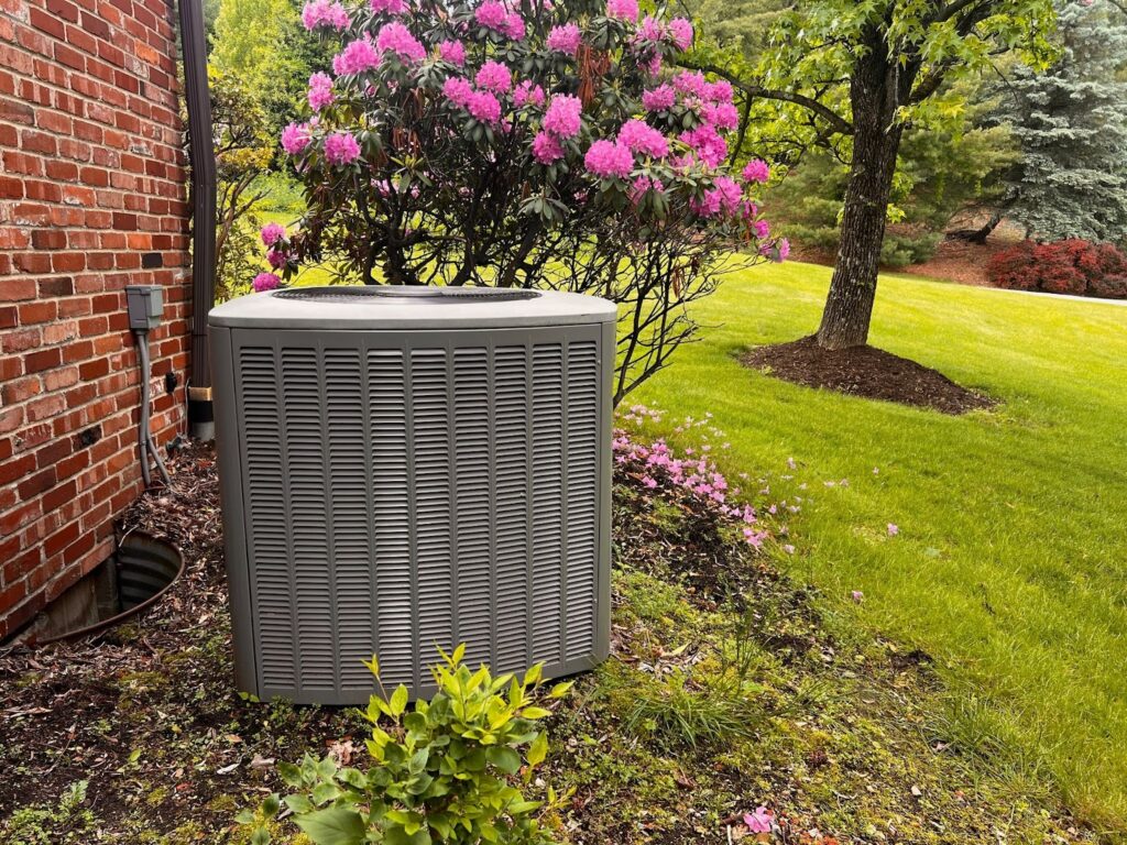 Outdoor AC condenser unit surrounded by spring landscaping ready for seasonal HVAC tune-up