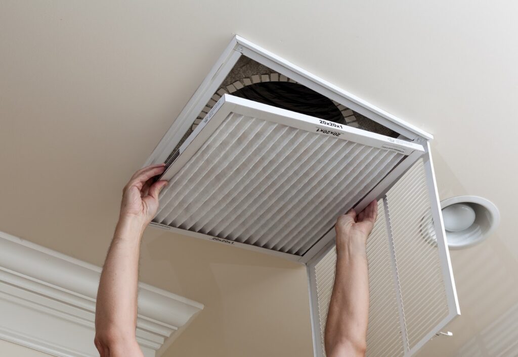 Homeowner removing a dirty air filter from a ceiling vent as part of a spring HVAC tune-up checklist