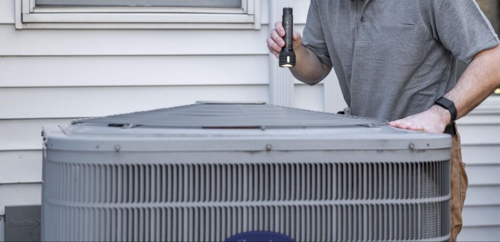 Technician inspecting an outdoor AC unit with a flashlight during HVAC service in Burbank, WA