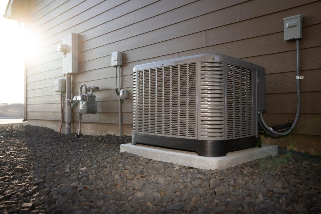 Outdoor central air conditioning condenser unit installed beside a home on a gravel yard.